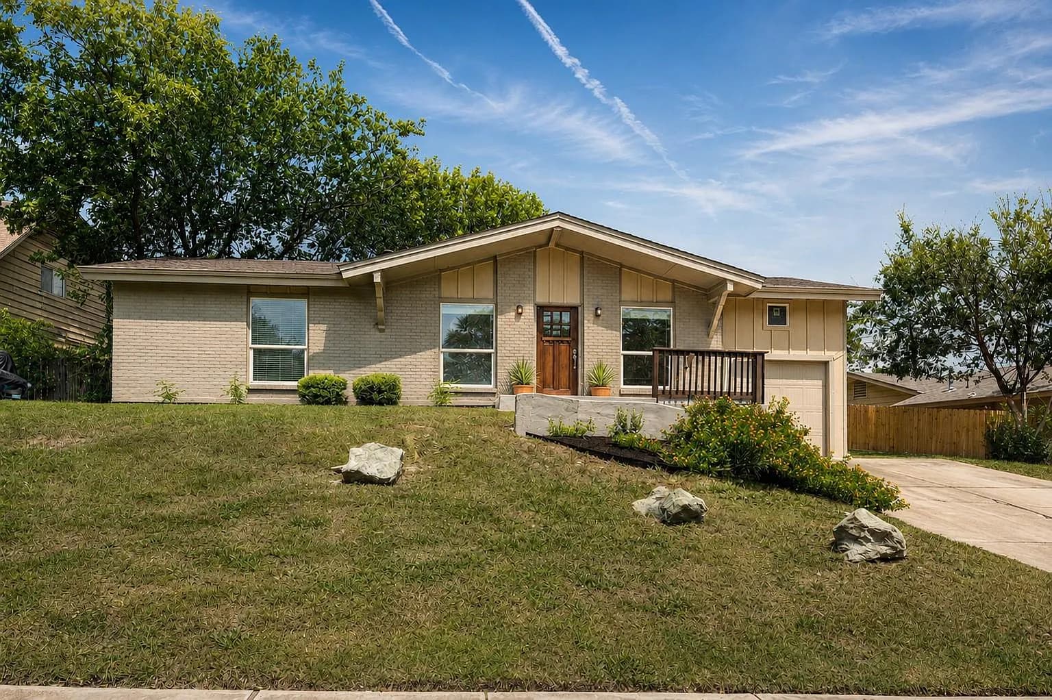 Front exterior of 2507 Glen Springs Way, a mid-century brick ranch home in Austin, Texas with a sloped roofline and landscaped front yard