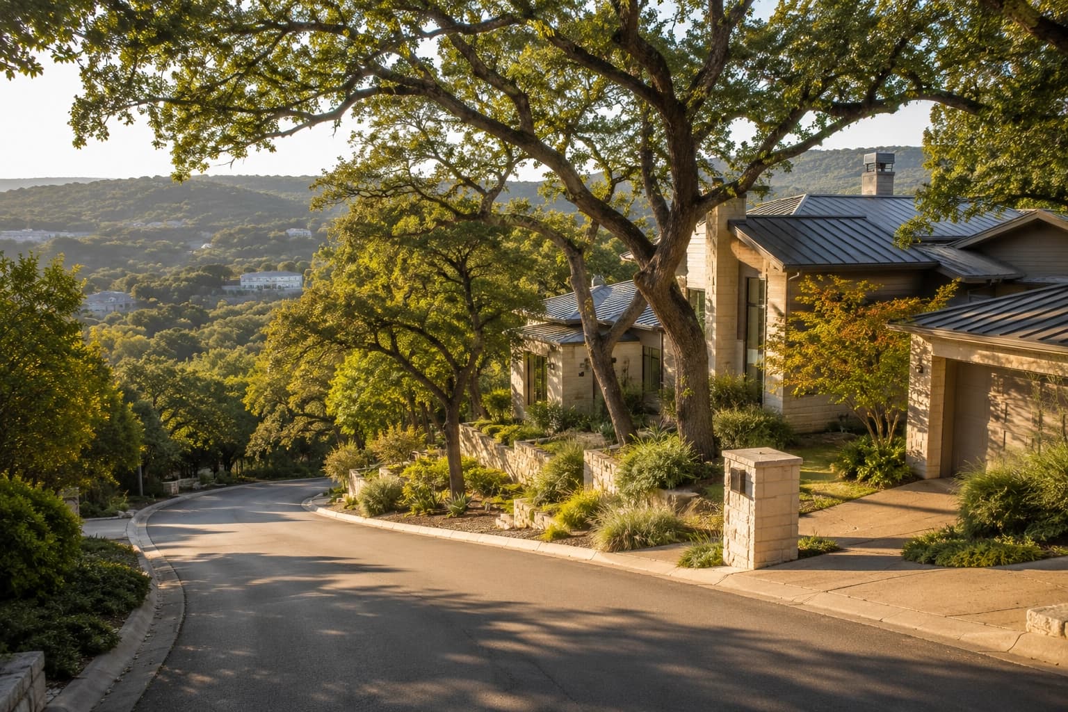Hillside residential street in Westlake Hills, Texas, with limestone homes tucked among mature oak trees and views of the Hill Country beyond in soft afternoon light